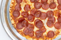 Overhead close-up of baked 60 min. Pan Pizza topped with pepperoni and melted cheese in a metal pan.