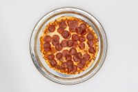 Overhead view of a whole 60 min. Pan Pizza topped with pepperoni on a metal pan.