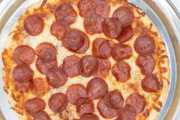 Overhead view of a 60 min. Pan Pizza with melted cheese and pepperoni slices in a metal pan.