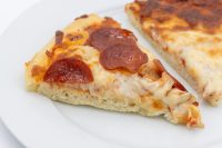 A slice of 60 min. Pan Pizza with melted cheese and pepperoni on a white plate.