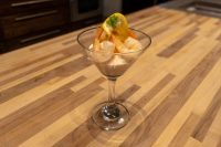 Shrimp Cocktail in a martini glass topped with a curled lemon slice and parsley sprig on a wood counter.