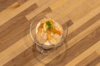 Overhead view of Shrimp Cocktail in a stemmed glass dish, with shrimp curled over a creamy pink sauce and topped with a lemon slice and parsley sprig, set on a striped wooden table