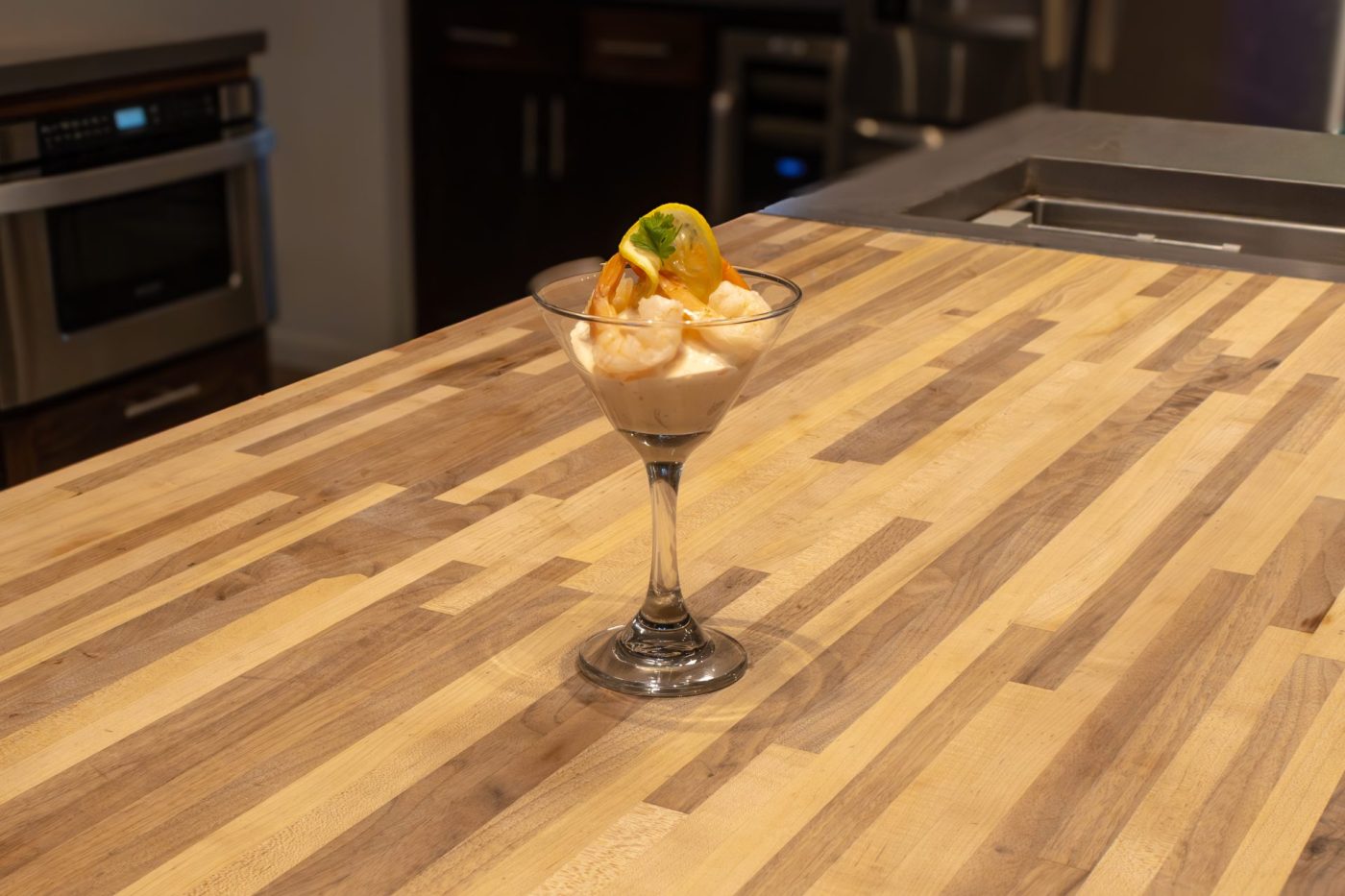A stemmed glass of Shrimp Cocktail with creamy sauce and a citrus garnish on a wooden countertop.
