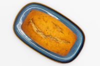 Baked Banana Bread loaf with a split top on a blue speckled ceramic platter.