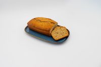 A loaf of Banana Bread with one slice cut, showing golden crust and beige crumb, on a blue plate.