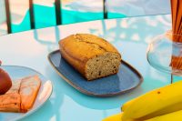 Sliced Banana Bread loaf on a blue plate with bananas on a light table.