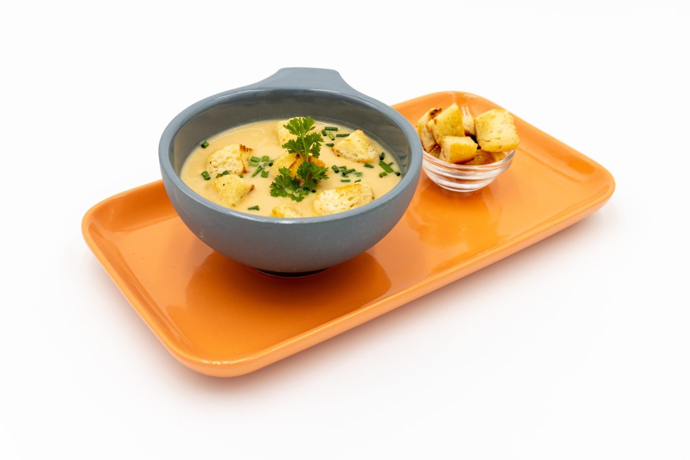 Bowl of Czech Garlic Soup Cesnecka with herb garnish, served with a side dish of croutons on an orange tray