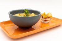 Bowl of creamy Czech Garlic Soup Cesnecka with parsley, served with roasted potato cubes on an orange tray.