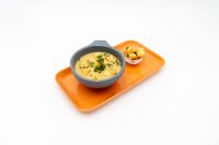 Bowl of Czech Garlic Soup Cesnecka with herbs and diced potatoes, served with a cup of croutons on an orange tray.