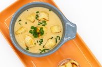 Bowl of Czech Garlic Soup Cesnecka topped with croutons, chives, and herb garnish on an orange tray