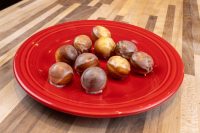 Nine glazed Donuts and Donut Holes, some dipped in chocolate, piled on a red plate.