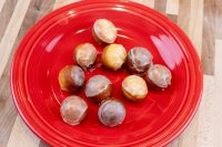 Ten glazed Donut Holes, some light and some darker, piled on a red plate on a wood counter