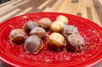 Glazed Donuts and Donut Holes dusted with powdered sugar, arranged on a red plate.