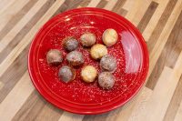 Ten glazed and powdered-sugar-dusted Donut Holes piled on a red plate, from the Donuts and Donut Holes recipe.