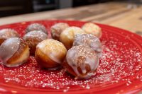 Glazed Donut Holes dusted with powdered sugar piled on a red plate