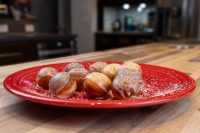 Red plate of Donuts and Donut Holes, glazed and dusted with powdered sugar on a wooden counter.