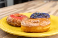 Three glazed Donuts on a yellow plate, one with red icing and sprinkles, one with dark sprinkled icing.