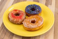 Three glazed donuts on a yellow plate, one with red sprinkles, one with dark sprinkles, one plain.