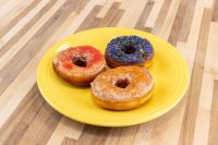Three glazed Donuts and Donut Holes—orange, blue with sprinkles, and plain—on a yellow plate.
