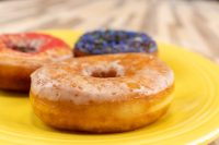 Three glazed Donuts and Donut Holes on a yellow plate, topped with red glaze and dark sprinkles.