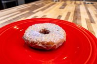 A glazed doughnut from Donuts and Donut Holes, topped with white sprinkles, on a red plate.