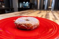 A glazed donut with colorful sprinkles from Donuts and Donut Holes sits on a red plate.