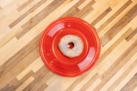 A single glazed donut with a sugary textured coating centered on a red plate atop a wood-plank table.