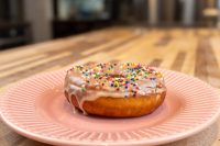 Glazed Donuts and Donut Holes with rainbow sprinkles and drips of glaze on a pink ridged plate