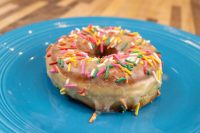 A glazed ring donut from Donuts and Donut Holes topped with rainbow sprinkles on a blue plate.
