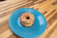 A glazed Donuts and Donut Holes topped with rainbow sprinkles on a blue plate atop a wooden table.