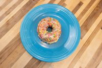 A glazed ring donut with rainbow sprinkles from the Donuts and Donut Holes recipe, on a blue plate.