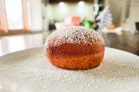 A powdered-sugar-dusted Czech Donuts Koblihy on a white plate with sugar scattered around it.