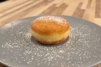A single fried Czech Filled Donuts Koblihy dusted with powdered sugar on a grey plate.