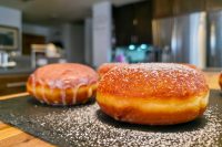 Two golden Czech Filled Donuts Koblihy, one glazed, dusted with powdered sugar on dark slate.