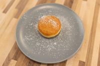 A single golden Czech Filled Donuts Koblihy dusted with powdered sugar on a gray plate.