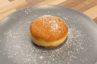 A single Czech Filled Donuts Koblihy with a glossy top dusted in powdered sugar on a grey plate.