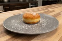 A golden Czech Donuts Koblihy dusted with powdered sugar on a gray plate atop a wooden countertop.