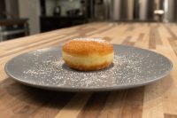 A fried Czech Filled Donuts Koblihy dusted with powdered sugar, filling visible at its seam, on a grey plate.