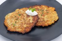 Two crispy Potato Pancakes Bramboraky on a black plate with sour cream and chopped chives on top.