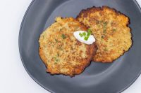 Two crispy Potato Pancakes Bramboraky on a dark plate topped with sour cream and chopped herbs.
