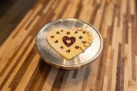 Heart-shaped Linzer Tart Hearts cookie with star cutouts showing red jam, dusted with sugar, on metal plate.
