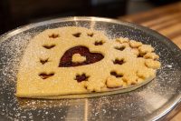 Heart-shaped Linzer Tart Hearts with red jam showing through cutout hearts, dusted with powdered sugar on a metal tray.