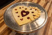Heart-shaped Linzer Tart Hearts with cut-out stars showing red jam, dusted with powdered sugar on a metal plate.