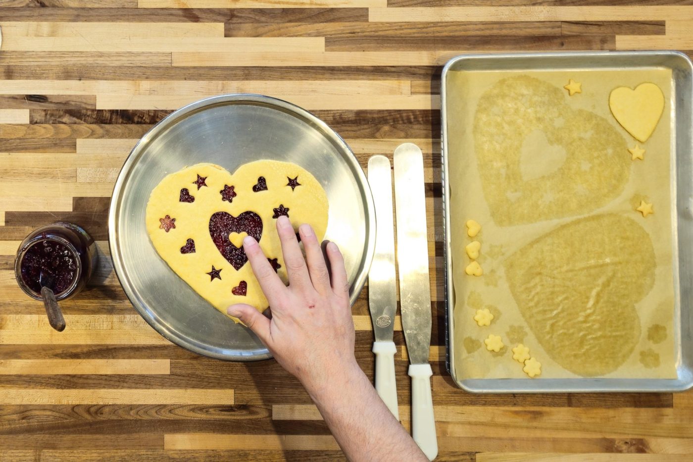 Hand presses a star-and-heart cut-out dough top onto a jam-filled Linzer Tart Hearts base.