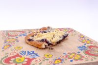 Slice of Sheet Kolach with Streusel showing streusel topping and dark berry filling on a painted wooden board.