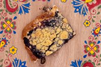 A broken piece of Sheet Kolach with Streusel showing dark blueberry filling and buttery crumb topping on a wooden board.