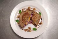 Halved Grilled Cheese with Goat Cheese and Beets on a white plate, garnished with walnuts, mint, and a sauce swirl.