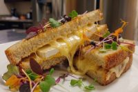 Halved Brie Grilled Cheese sandwich oozing melted cheese, topped with microgreens and edible flowers.