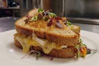Brie Grilled Cheese sandwich with melted cheese oozing from toasted bread, garnished with microgreens on a white plate.