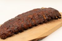 A charred, glazed rack of American BBQ – Honey Pork Ribs resting on a wooden cutting board.
